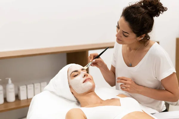 Esthétique appliquer un masque sur le visage d'une femme d'âge moyen dans le centre de bien-être moderne. — Photo