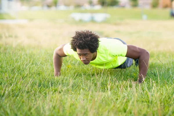 Schwarzer Mann macht Liegestütze und trainiert seine Brust auf dem Rasen eines Stadtparks. — Stockfoto