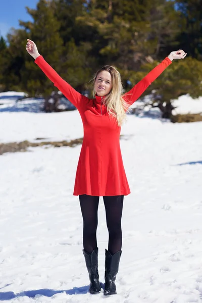 Frau in rotem Kleid und schwarzen Strümpfen öffnet ihre Arme vor Glück in den schneebedeckten Bergen. — Stockfoto
