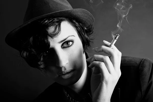 Brunette woman smoking a cigarette on black background wearing a — Stock Photo, Image