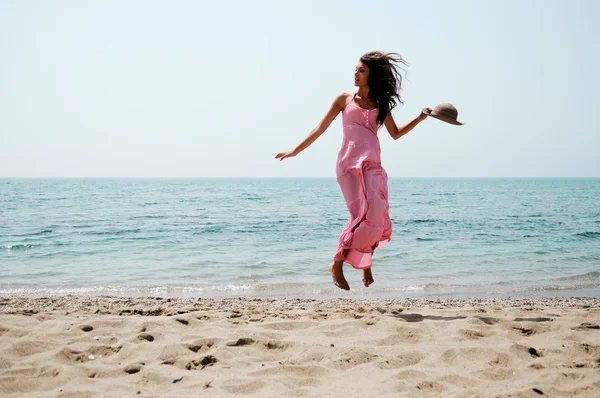 Mooie vrouw met lang roze jurk springen op een tropisch strand — Stockfoto