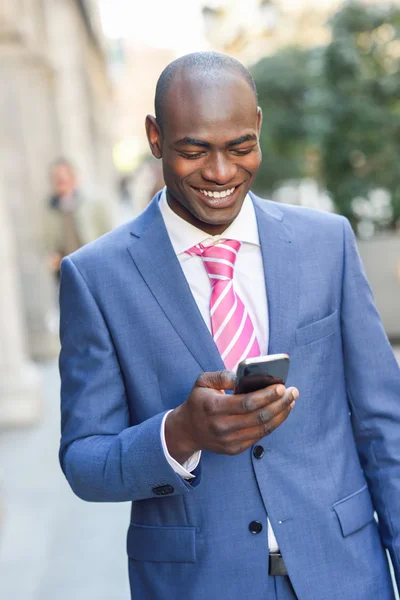 Uomo d'affari nero che legge il suo smartphone in background urbano — Foto Stock