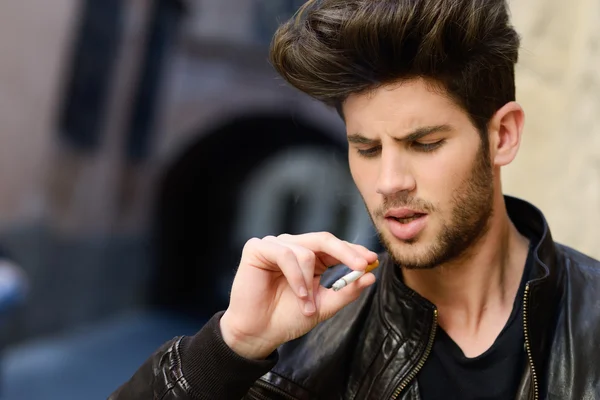 Jovem fumando um cigarro no fundo urbano — Fotografia de Stock