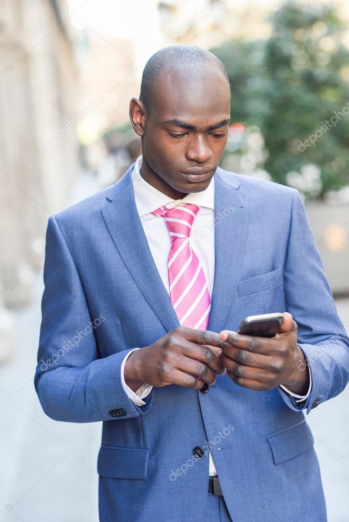 Black businessman reading his smartphone in urban background