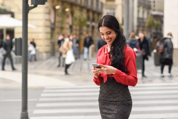 Латиноамериканская стюардесса на городском фоне смотрит на свой мобильный телефон — стоковое фото