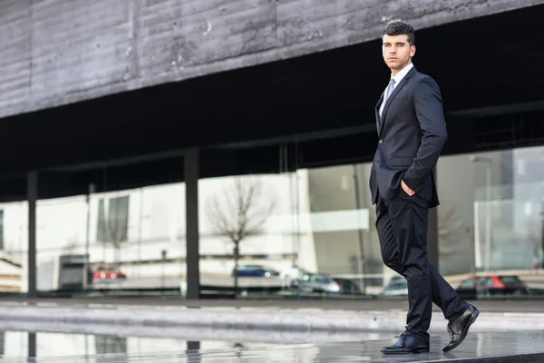 Jovem empresário perto de um prédio de escritórios usando terno preto — Fotografia de Stock