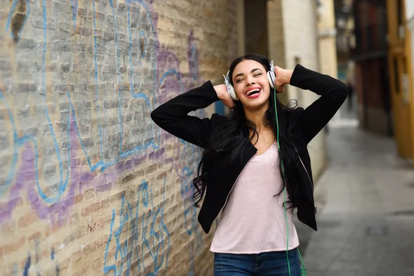 Vrouw in stedelijke achtergrond muziek met een hoofdtelefoon beluisteren — Stockfoto