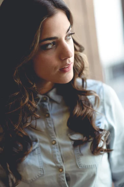 Beautiful young woman looking through the window — Stock Photo, Image