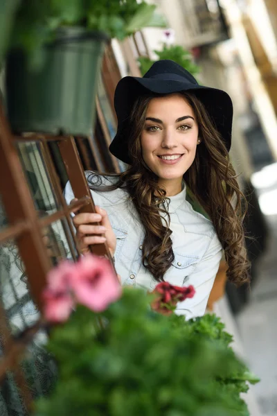 Mujer joven con sombrero en el fondo urbano con ropa casual — Foto de Stock