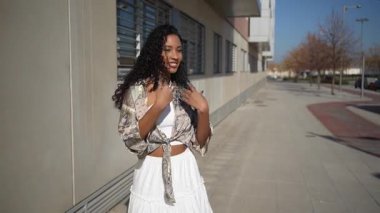 Neşeli ve şık bir kıyafet giymiş neşeli genç bir kadın güneşli bir şehir sokağında geziniyor, güven ve mutluluk saçıyor, zahmetsizce anın neşesini kucaklıyor.