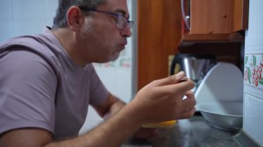 Tatmin olmuş bir adam, lezzetli yemeğinin her bir ısırığını neşeye boğulmuş sıcak bir mutfak tezgahında yer. Bu sahne, konfor getiren lezzetli ev yemeklerinin özünü yakalar.