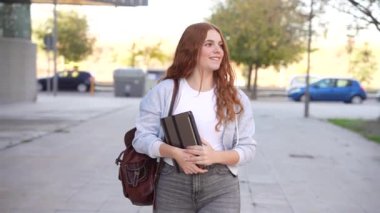 Genç bir kadın, önlerindeki verimlilik ve fırsatlarla dolu bir güne hazırlanırken gündelik defterlerini taşıyarak canlı ve modern bir şehir ortamında güvenle geziniyor.