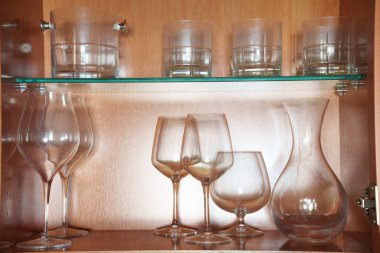 Kırsal ahşap raflarda sofistike şarap seti şarap kadehleri ve sürahiler ahşap raf ünitesinde hafifçe aydınlatılmış.