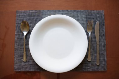 Klasik çatal bıçak düzeniyle sade seramik tabak, minimalist bulaşık takımı ve sıcak doğal ışıklandırmayla serenat masası davetkar