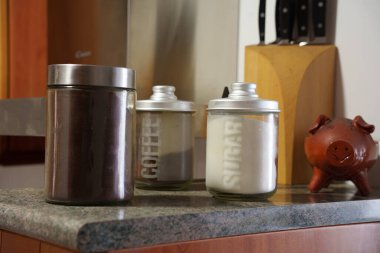 Kırsal mutfak tezgahı, kahve kavanozları ve şeker kutusu, kahverengi metal teneke, eski seramik domuz kumbarası, ahşap bıçak bloğu, yumuşak sıcak aydınlatma