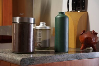 Modern mutfak tezgahı yeşil şişe ve kahve kavanozu etiketli şeker kutusu ve benekli cam şişe bıçak bloğunun yanındaki kahverengi teneke, seramik domuz kumbarasının yerini alıyor.,