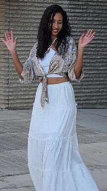A graceful woman elegantly showcasing a stunning bohemianinspired outfit, which includes a beautifully floral top paired with a flowing white skirt, all against a rich and textured backdrop