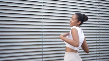 Modaya uygun bir bluz ve akıcı etek giyen neşeli bir kadın, hareket ederken bulaşıcı bir neşe, özgürlük ve enerjik bir enerji yayarak modern bir duvarın karşısında zarif bir şekilde dans ediyor.