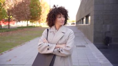 Modaya uygun bir kadın şık bir kıyafetle dışarıda duruyor. Parlak gün ışığıyla dolu güzel bir günde, göz kamaştırıcı, çağdaş bir mimarinin arka planına karşı şık tarzını sergiliyor.