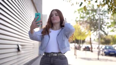 Uzun, dalgalı kızıl saçlı neşeli genç bir kadın telefonuyla konuşurken keyifli bir yürüyüş yapıyor. Pürüzsüz, modern bir binanın önünde duruyor.