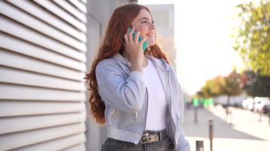 Parlak bir gülümsemesi olan genç bir kadın açık havada şehir merkezinde gündüz saatlerinde kaygısız ve sıradan bir yaşam tarzını gözler önüne sererken akıllı telefonuyla mesajlaşırken görülüyor.