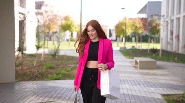 Moda ve modaya uygun genç bir kadın kendine güvenerek canlı bir şehir parkında yürüyor, çarpıcı pembe bir ceket ve şık siyah pantolon ile modern tarzını güzel bir şekilde sergiliyor.