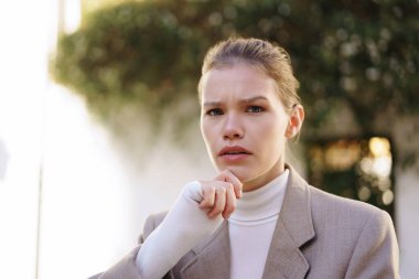 Sofistike giyinmiş düşünceli bir iş kadını, özgüvenini, hırsını ve özel profesyonelliğini somutlaştıran düşünceli bir ifadeye sahiptir.