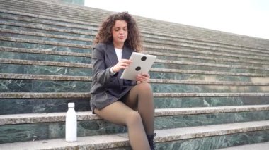 Modern profesyonel bir kadın bir tablet kullanarak taş basamaklarda oturur, verimliliğini ve yaratıcılığını ateşleyen açık hava ortamının tadını çıkarırken iş ve yaşam arasındaki dengeyi gözler önüne serer.