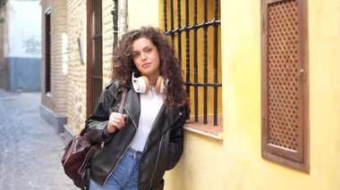 Canlı bir caddede, şehvetli kıvırcık saçlı, şık deri ceketli ve parlak kulaklıklı, moda anlayışını gözler önüne seren modacı bir kadın...