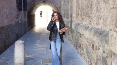 Zarif deri ceket giyen şık ve şık bir kadın büyüleyici, pitoresk tarihi bir sokakta kendine güvenerek poz veriyor ve eşsiz şehir moda anlayışını güzel bir şekilde sergiliyor.