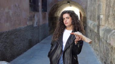 Kendine güvenen genç bir kadın, kendine güvenen dar bir şehir geçidinde, kendine has tarzını şık bir deri ceketle sergileyerek lezzetli bir atıştırmalık tutarken, güzel bir şekilde duruyor.