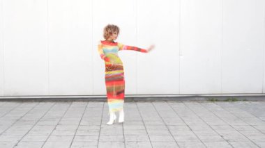 Çarpıcı bir model, modern tarz ve moda kültürünün özünü mükemmel bir şekilde somutlaştıran minimalist beyaz bir duvara karşı canlı, çarpıcı ve güzel çizgili bir elbise sergiliyor.