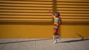 Moda mankeni, parlak ve çarpıcı sarı bir duvarın önünde göz alıcı dinamik bir poz verir. Renkli kıyafetini sergiler ve kendine güvenen, canlı bir stil sergiler.