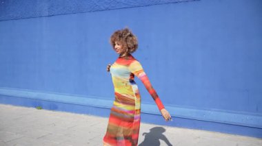 Modaya uygun bir insan çarpıcı derecede canlı mavi bir duvara karşı zarif bir duruş sergiliyor, çarpıcı ve renkli bir elbise sergiliyor, etrafındaki canlı atmosferi güzelleştiriyor.