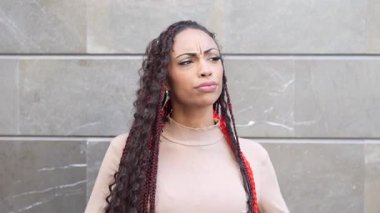 Uzun, güzel örgülerle süslenmiş şık ve kendine güvenen bir manken zarif ve modern bir duvara, mükemmel bir şekilde modern tarzda ve büyüleyici bir şekilde poz veriyor.