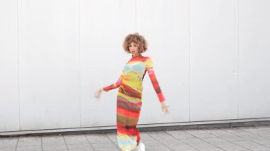 Canlı bir şehirde, kendine güvenen bir model, son moda eğilimlerini sembolize eden ve modern bireyler için çağdaş şıklığı somutlaştıran, karmaşık desenli canlı bir elbise içinde poz verir.