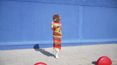 Göz kamaştırıcı ve şık bir model, canlı, renkli bir elbiseyi canlı mavi bir arka plana, hiç şüphesiz zarafet, güven ve zerafeti her yönüyle sergiliyor.