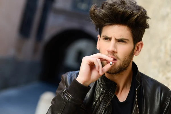 Young man smoking a cigarette in urban background — Stock Photo, Image