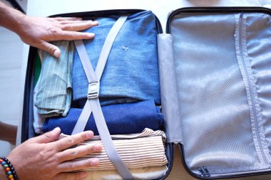 El çantası katlanmış kıyafetler, kot pantolon, örgü kazak, hasır şapka, ağ cebi açık, dikkatli katlama, bileğinde boncuklu bilezik, parlak doğal