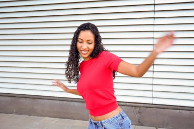 Dalgalı kolları ve gülüşü olan dans eden kadın, bol kotlu kırmızı bluz, metal deklanşöre karşı dinamik hareket, bulanık hareket ve enerjik hareket.