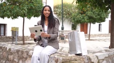 Modern teknolojinin ve doğanın sakinliğinin karışımını vurgulayarak büyüleyici ve neşeli bir atmosfer yaratan, güzel bir açık hava ortamında tabletle meşgul olan zarif genç bir kadın.