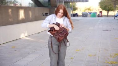 Moda kıyafetleri içinde genç bir kadın şık sırt çantasıyla açık havayı keşfediyor, neşeli şehir ortamında geziniyor ve kaygısız bir macera ruhunu somutlaştırıyor.