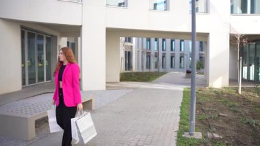 Canlı pembe paltolu şık bir kadın dikkat çeken çarpıcı bir mimari ve canlı bir atmosferle dolu modern şehir manzarasında güvenle yürüyor.