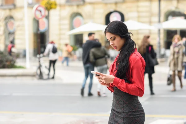 Hispanische Stewardess im urbanen Hintergrund schaut auf ihr Handy — Stockfoto