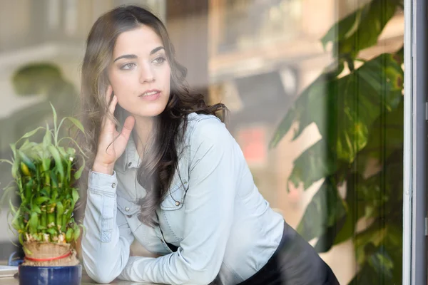 Woman sitting indoor in urban cafe looking through the window — Stock Photo, Image