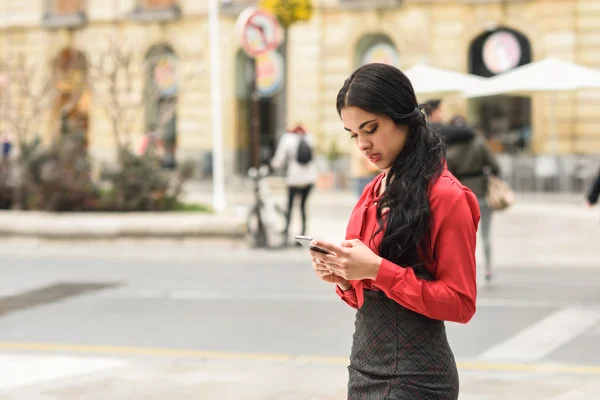 Латиноамериканская стюардесса на городском фоне смотрит на свой мобильный телефон — стоковое фото