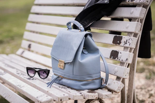 Bag, sunglasses and leather jacket on a bench — Stockfoto