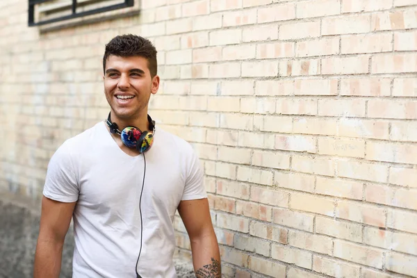 Jonge man in stedelijke achtergrond muziek met een hoofdtelefoon beluisteren — Stockfoto