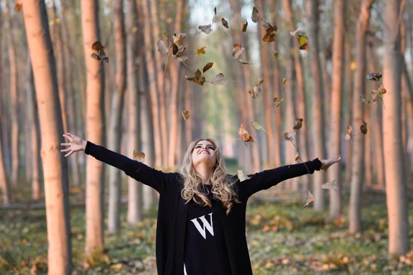 Mulher feliz brincando com folhas de outono na floresta — Fotografia de Stock
