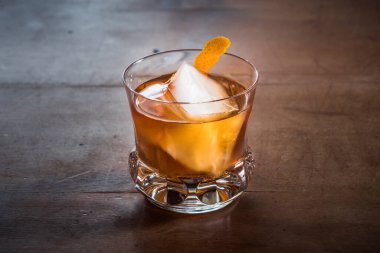 Old Fashioned Cocktail with Whiskey on a Wood Table with Orange Twist in a Slegant, Retro Crystal Tumbler